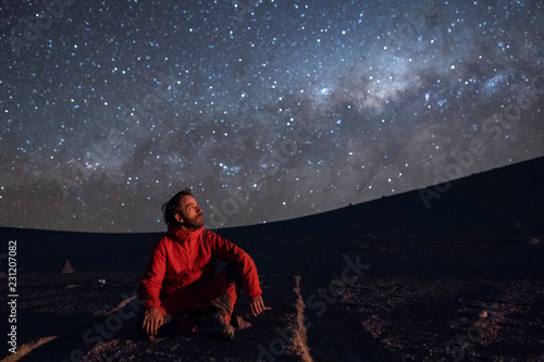A young adult man seating and looking at the view of our Milky Way galactic core located in the constellation of Sagittarius, an amazing view at Atacama Desert. Chile
