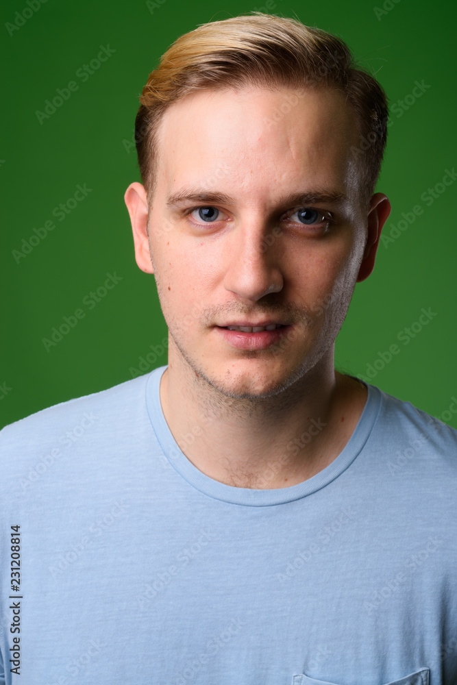 Fototapeta premium Young handsome man with blond hair against green background