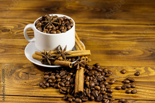 Coffee beans in white cup, cinnamon sticks and star anise on wooden table