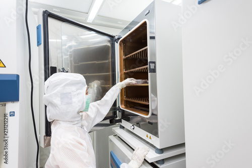 A scientist in sterile coverall gown placing cell culture flasks in the CO2 incubator. Doing biological research in clean environmental. Cleanroom facility