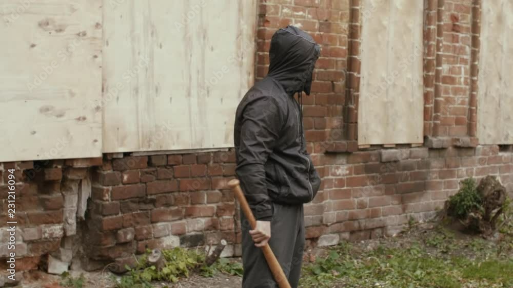 Aggressive bandit in black mask and hood ganging with baseball bat outdoors Aggressive bandit in black mask and hood ganging with baseball bat outdoors