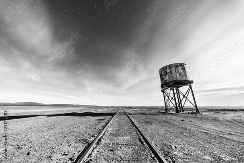 Old and abandoned railway track and station with it water tank to fill the trains during their travel around the Atacama Desert for transporting niter coming from the mining industry, full moon scene