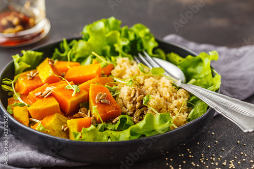 Warm quinoa and pumpkin salad in a white plate on dark background.