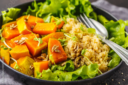 Warm quinoa and pumpkin salad in a white plate on dark background.