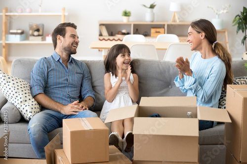 Young multi-ethnic family celebrate move at new modern wealthy home sitting together on couch in living room laughing smiling having fun clapping hands. First dwelling relocation and mortgage concept © fizkes