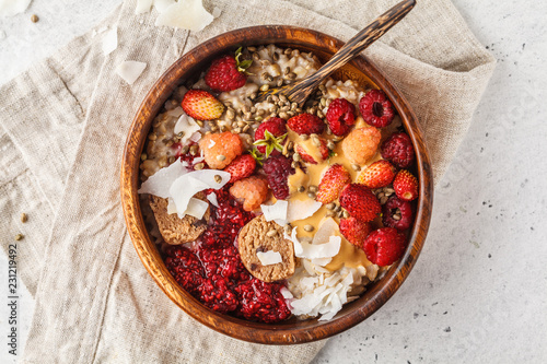 Trendy vegan bowl of oatmeal porridge with berries, raw vegan balls and peanut butter.