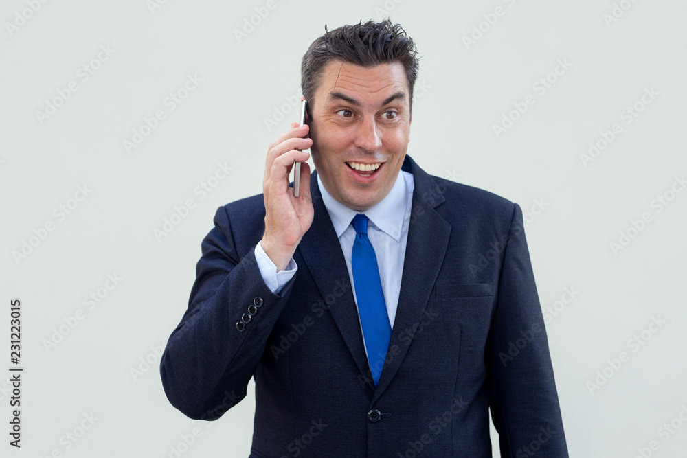 Cheerful male executive leaning communication on phone and looking away. Positive businessman in suit using mobile phone. Conversation concept Cheerful male executive leaning communication on phone and looking away. Positive businessman in suit using mobile phone. Conversation concept