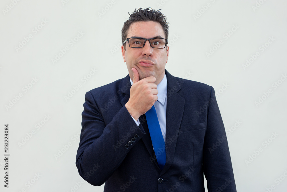 Confused handsome businessman thinking about project. Puzzled man in suit rubbing chin and looking at camera. Interest concept Confused handsome businessman thinking about project. Puzzled man in suit rubbing chin and looking at camera. Interest concept