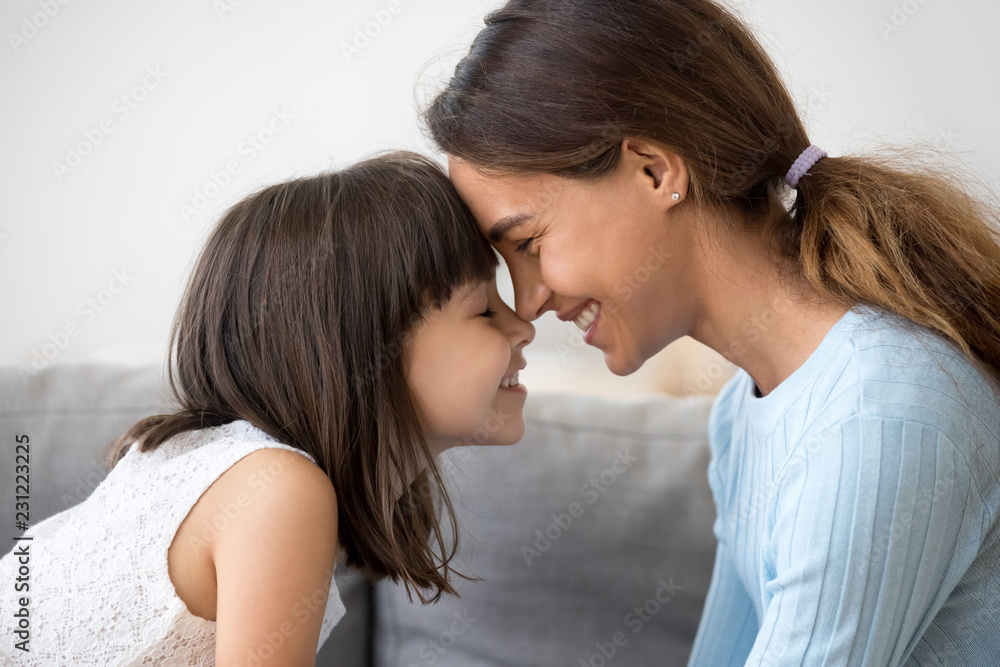 Close up profile faces smiling mother and daughter touching with foreheads with closing eyes. Mom expressing understanding candid emotions and love to sweet little child. Happy friendly family concept Close up profile faces smiling mother and daughter touching with foreheads with closing eyes. Mom expressing understanding candid emotions and love to sweet little child. Happy friendly family concept