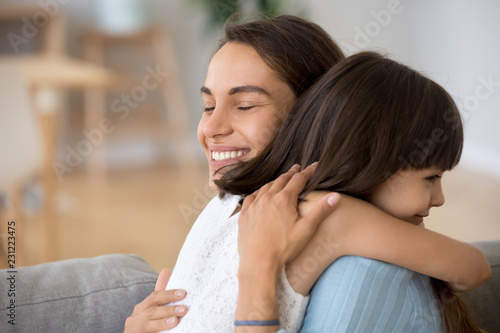 Close up candid mother hugging daughter expressing love and tender. single mom embrace little kid sitting together on couch spend time together at home. Happy friendly wellbeing family concept
