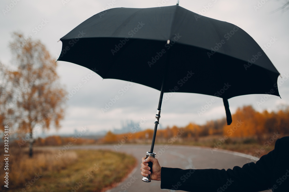 Young man in black holding umbrella.