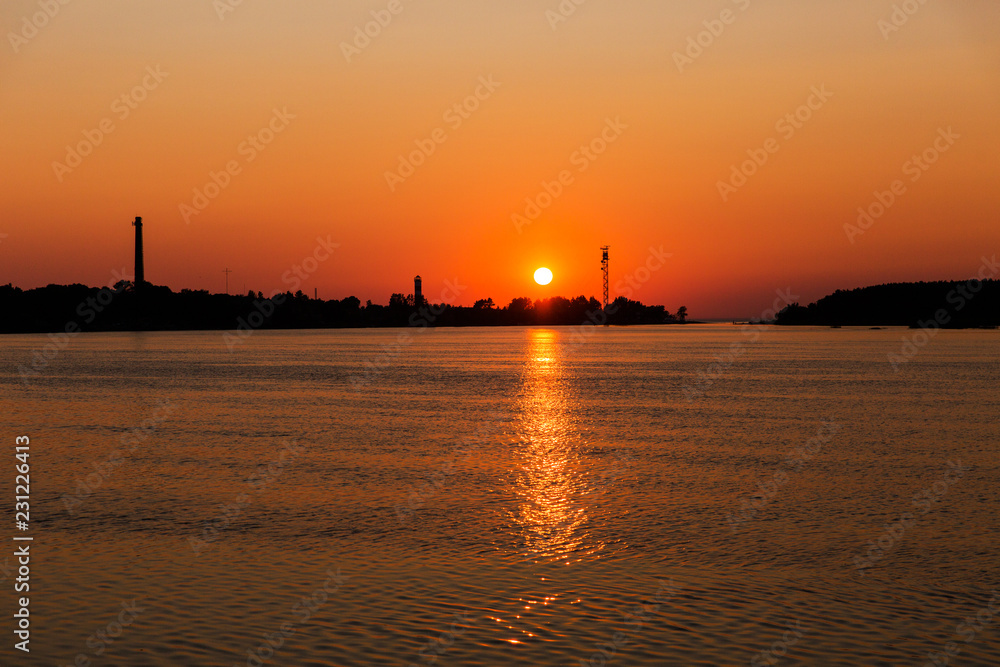 Beautiful sunset on the river. Silhouette of industrial city. Orange sun in the sky Beautiful sunset on the river. Silhouette of industrial city. Orange sun in the sky
