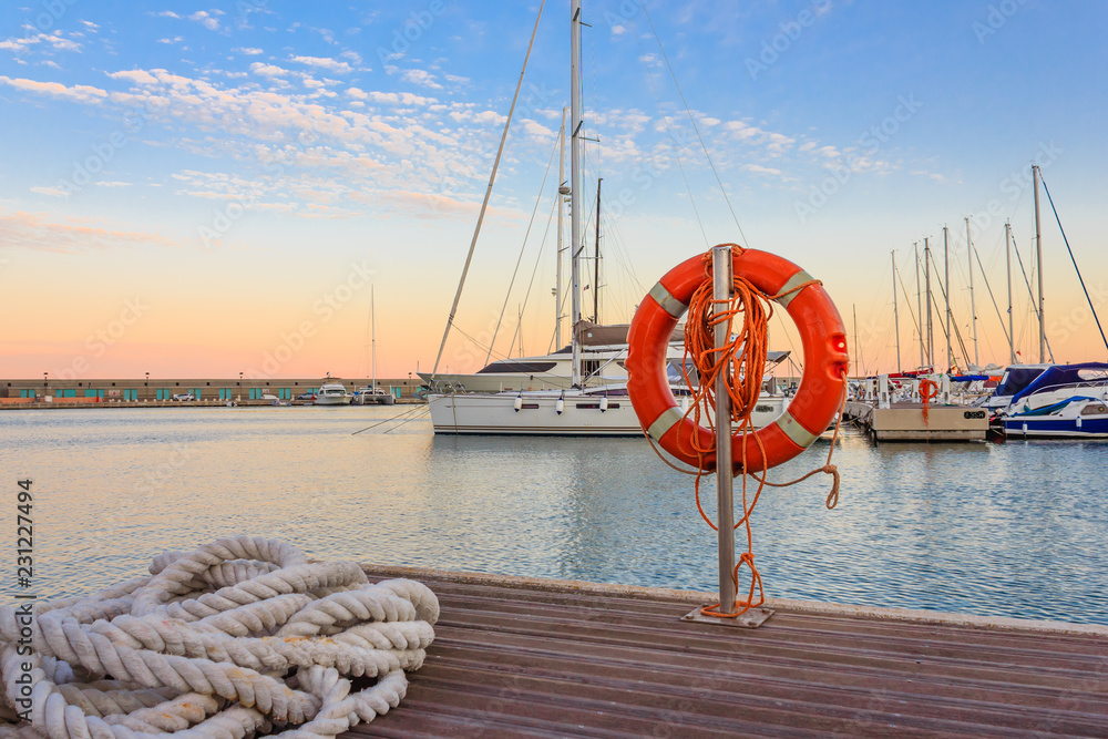Obraz premium the quay of a marina at the sunset /a mooring rope with a lifebelt on the quay of a marina at the sunset