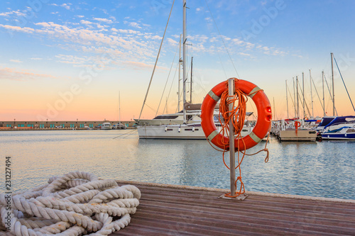Fotografia the quay of a marina at  the sunset /a mooring rope with a lifebelt  on  the qua