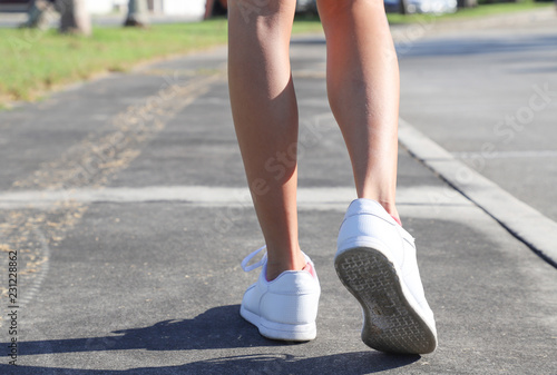 female legs in sneakers close up running down the road in the morning