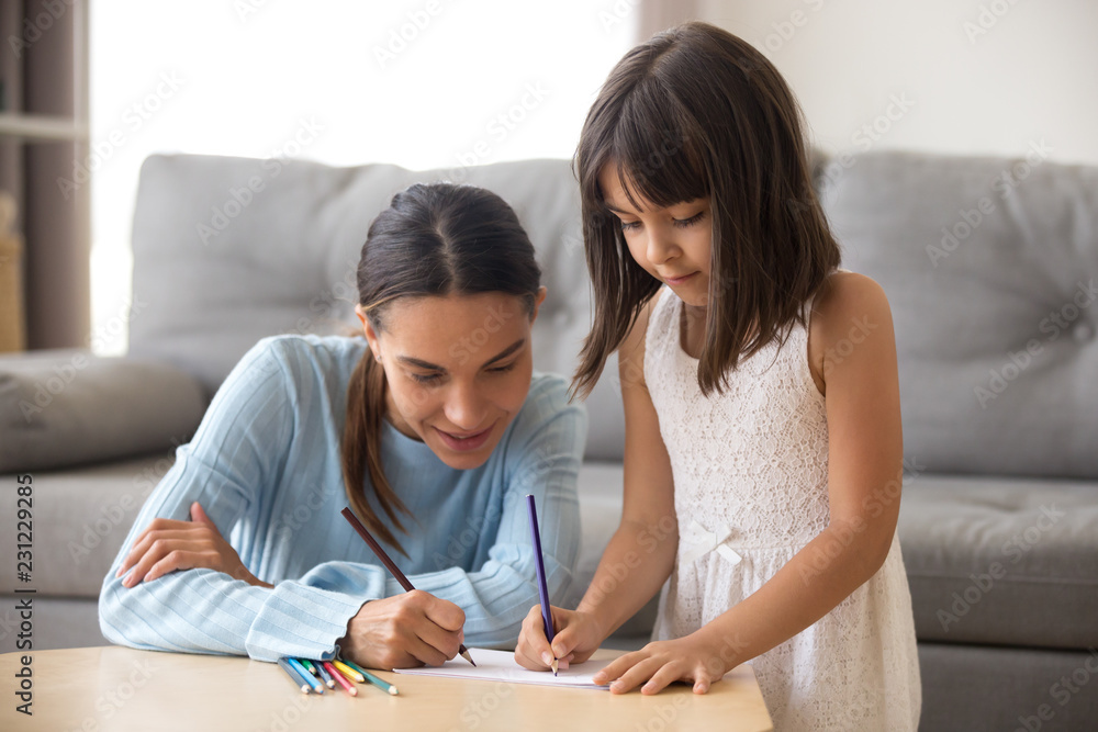 Single mother and preschool daughter have fun drawing on paper at table with colored pencils in living room at home or child nurse spend time with adorable girl. Creative family activities concept Single mother and preschool daughter have fun drawing on paper at table with colored pencils in living room at home or child nurse spend time with adorable girl. Creative family activities concept