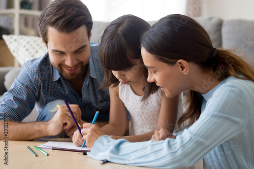 Happy multi-ethnic family have fun spend time together at home. daughter mother and Caucasian father drawing on paper sitting at table with coloured pencils closeup. Leisure activities concept