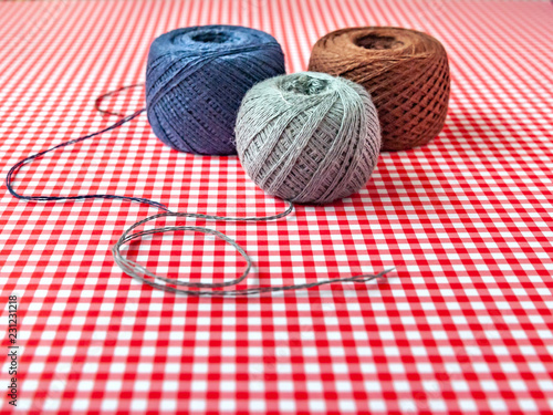 Multicolored spools of cotton thread on a red checkered background. Selective focus, space for text.
