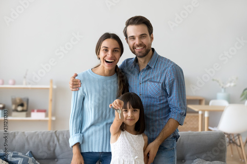Diverse family at new home. Little preschool daughter holds in hand keys standing with young parents mother and father in living room smiling looking at camera. Moving relocate at new house concept © fizkes