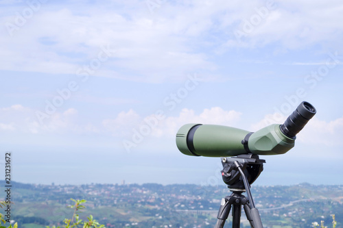 Green spotting scope or monocular at mountain top against the background of a mountain landscape in summer day. Observation of birds, birdwatching photo