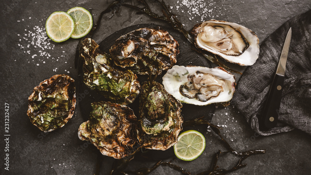 Fresh opened oysters with lemon, spices, salt, a knife and seaweed on slate stone background. Seafood, Shellfish, toning, top view Fresh opened oysters with lemon, spices, salt, a knife and seaweed on slate stone background. Seafood, Shellfish, toning, top view