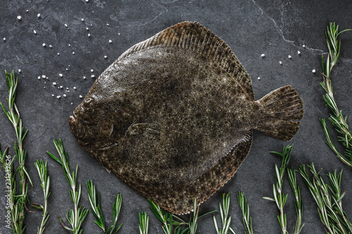Valokuvatapetti Raw whole flounder fish with rosemary on dark stone background