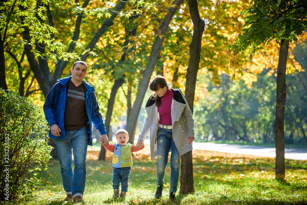 Beautiful young family on a walk in autumn forest on maple yellow trees background. Father and mother hold son on hands. Happy family leisure together concept Beautiful young family on a walk in autumn forest on maple yellow trees background. Father and mother hold son on hands. Happy family leisure together concept