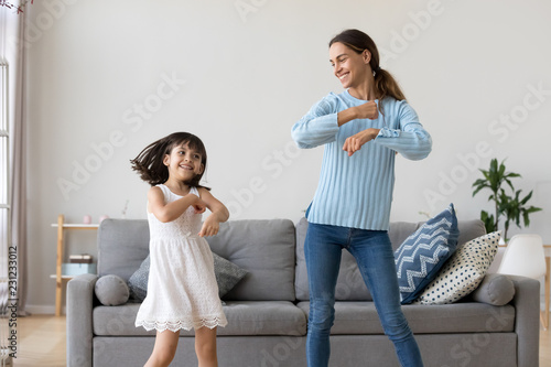 Принти на полотні Cheerful mother little daughter standing in living room at home moving dancing to favourite song together