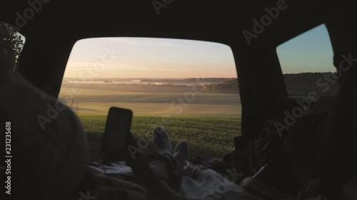 Wallpaper Mural Woman admiring the sunrise in trunk of car. Girl dressed in woolen clothes reading and texting massages on mobile phone against backdrop of forest panorama in fog . View from inside slow motion video Torontodigital.ca