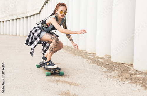 young girl with tattoo rides on a longboard