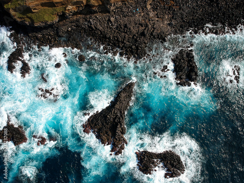 Aerial top view of sea waves hitting black volcanic rocks on the coastline with turquoise sea water. Amazing rock cliff seascape in the Portuguese coastline. Azores islands. Drone shot. © nvphoto