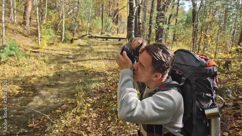 Traveler photographing scenic views in forest by mountain river. Man shooting picturesque views. The guy takes photo and video on old retro camera on film. Professional photographer traveler. Traveler photographing scenic views in forest by mountain river. Man shooting picturesque views. The guy takes photo and video on old retro camera on film. Professional photographer traveler.
