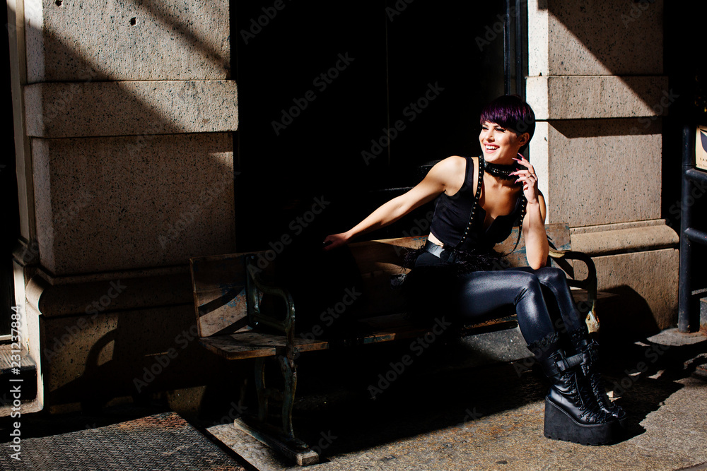 Portrait of a beautiful young woman in a black leather outfit smiling and sitting on a bench Portrait of a beautiful young woman in a black leather outfit smiling and sitting on a bench