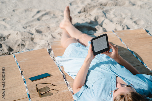 Frau liest mit E-Book Reader am Strand