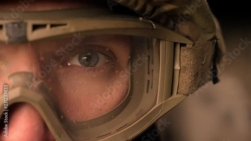 Close-up focused eye of strong military man in uniform and helmet, looking at camera while standing, authentic modern appearance