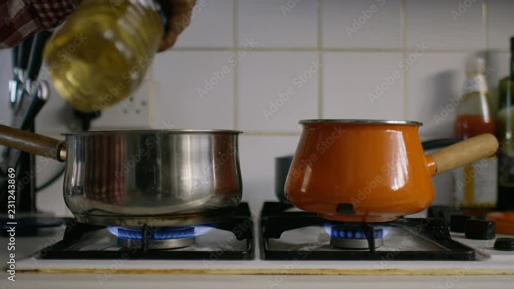 Woman pouring cooking oil into a pot on a heated stove Woman pouring cooking oil into a pot on a heated stove