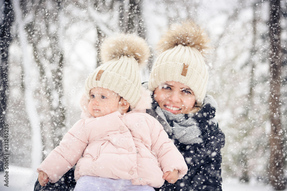 Cute little baby girl with mother wearing winter hat outside on a snowing day in winter