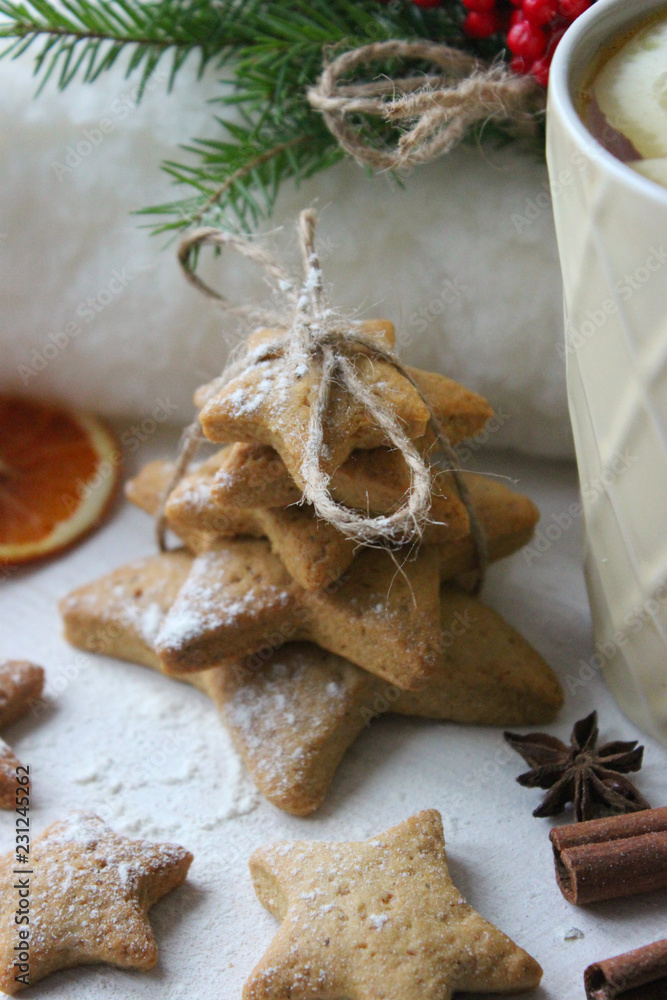A Cup of tea with lemon on the table close-up surrounded by Christmas decorations and homemade cakes. Star shaped gingerbread, cinnamon sticks and dried oranges on white background.