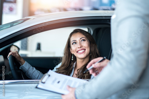 Happy customer buying brand new car at local car dealership. Car salesman with contract and the buyer.