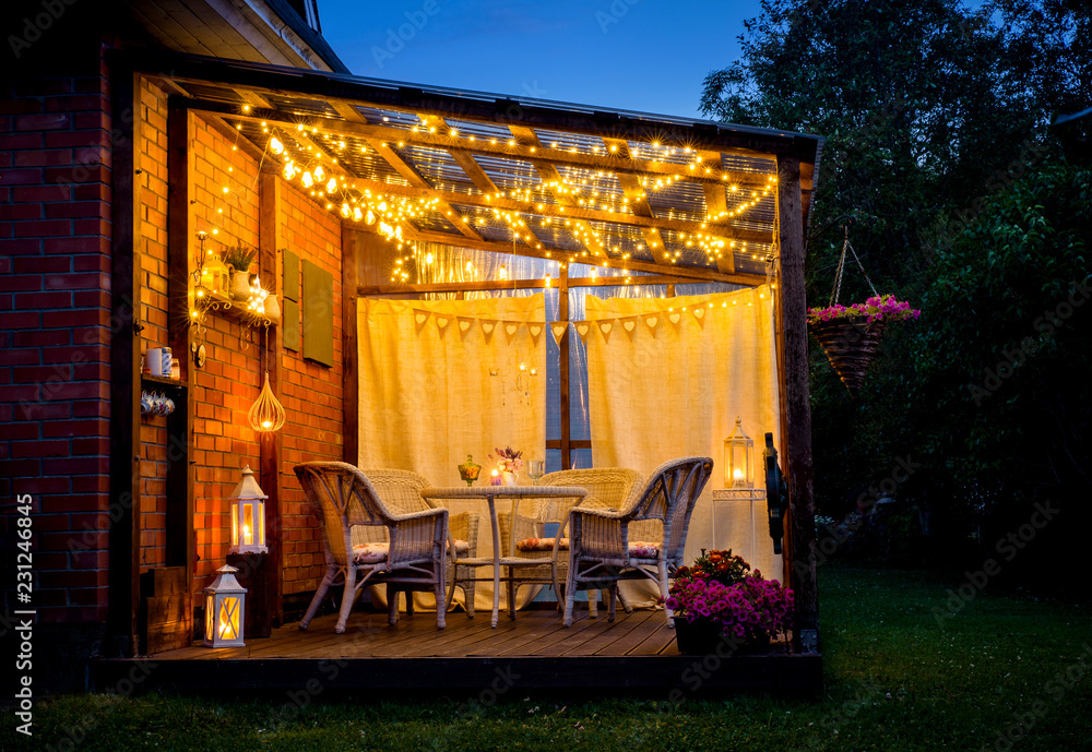 View over cozy outdoor terrace with table and chairs, very romantic  lighting, white lanterns, candles burning, led string party lights and  bulbs with star effect, in the evening. Stock Photo | Adobe