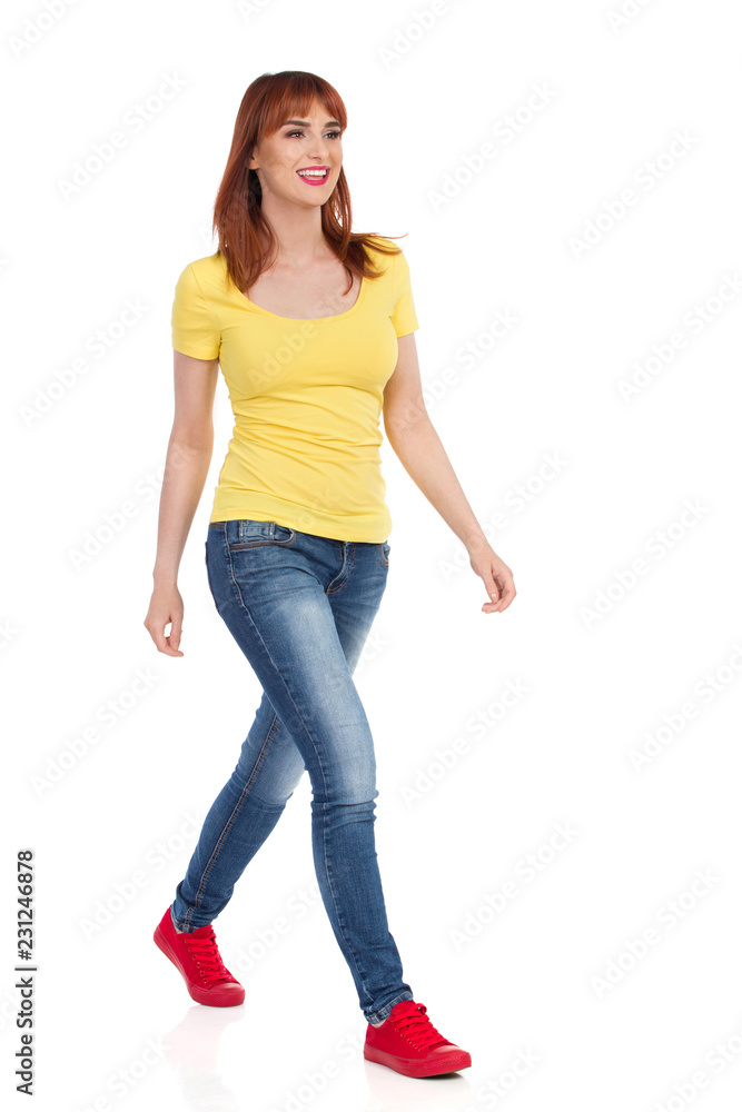 Young Woman In Yellow Shirt, Jeans And Red Sneakers Is Walking And Looking Away Young Woman In Yellow Shirt, Jeans And Red Sneakers Is Walking And Looking Away