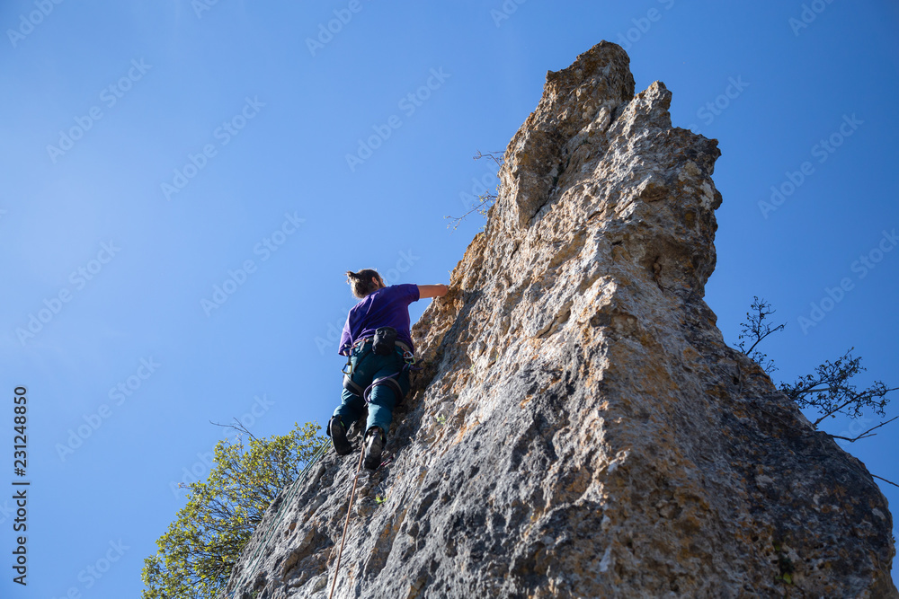 From below shot of male climber climbing mountain wall on amazing sunny day 