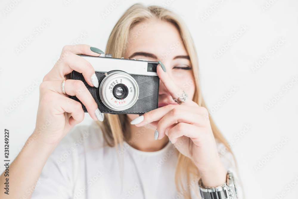 Portrait of a young stylish blonde girl using and taking pictures on an old vintage camera on a white background Portrait of a young stylish blonde girl using and taking pictures on an old vintage camera on a white background