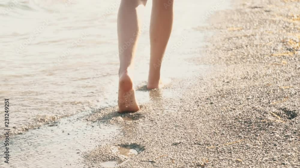 Close-up view of woman's legs walking on the pebble beach. Close-up view of woman's legs walking on the pebble beach.