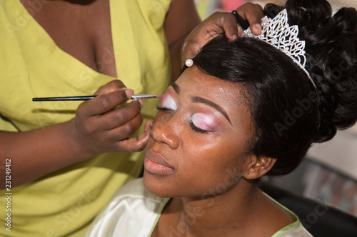 Model young pretty american black woman getting her eyes make up done by professional artist using brush applying eyeshadow for wedding celebration