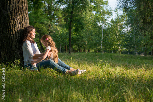 Mom and daughter are sitting near a tree