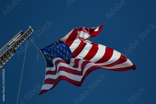 Sunlit  Close View of American Flag Waving from Crane Boom Against Vibrant Blue Sky, No Clouds photo