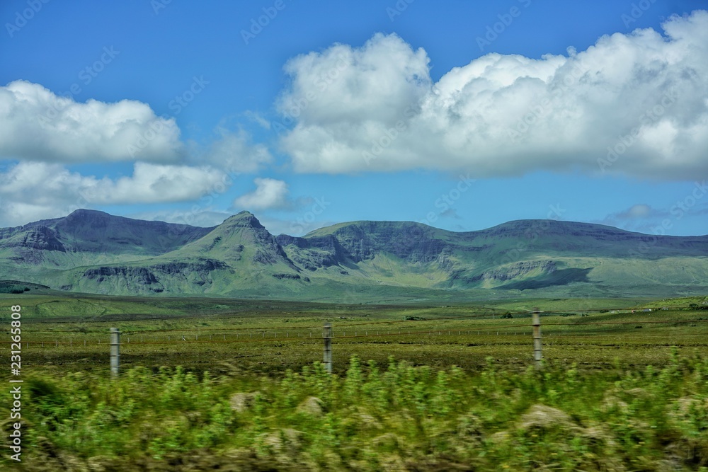 Weitläufige grüne Weidelandsschaft führt zu einer weichen Berglandschaft darüber blauer Himmel mit weissen Wolken Schottland