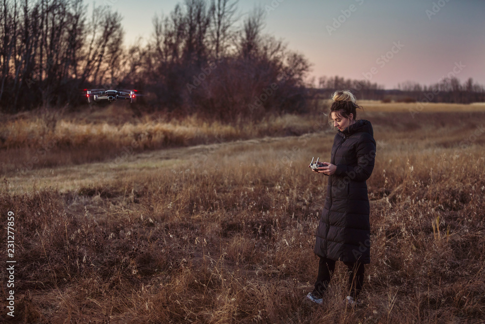 Female drone pilot looks at her remote controller while operating in a field during autumn at dusk. Female drone pilot looks at her remote controller while operating in a field during autumn at dusk.