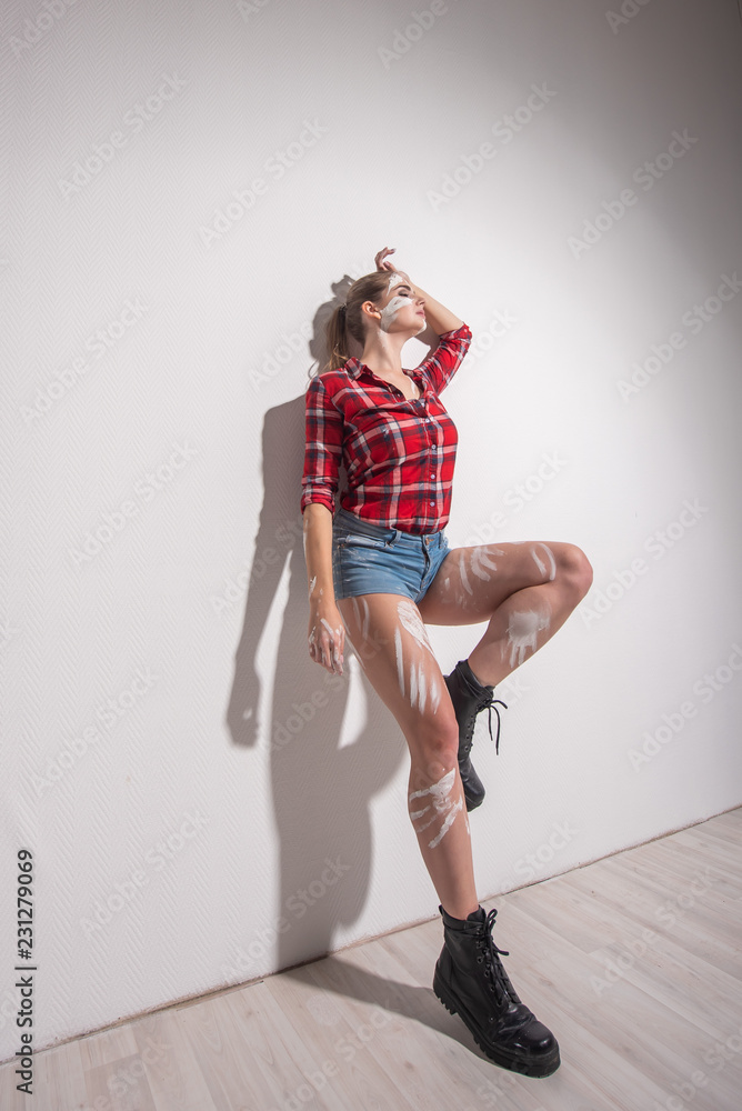 A beautiful young woman soiled in white paint is leaning against the wall. The girl in shorts paints the wall. A beautiful young woman soiled in white paint is leaning against the wall. The girl in shorts paints the wall.